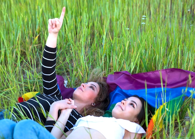 Foto dos chicas lesbianas tirado en el pasto con la bandera del orgullo gay