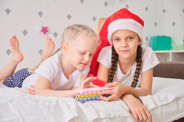 Dos chicas lindas se acuestan en la cama y juegan juegos de teléfonos inteligentes, concepto de vacaciones de Navidad, videollamadas a familiares