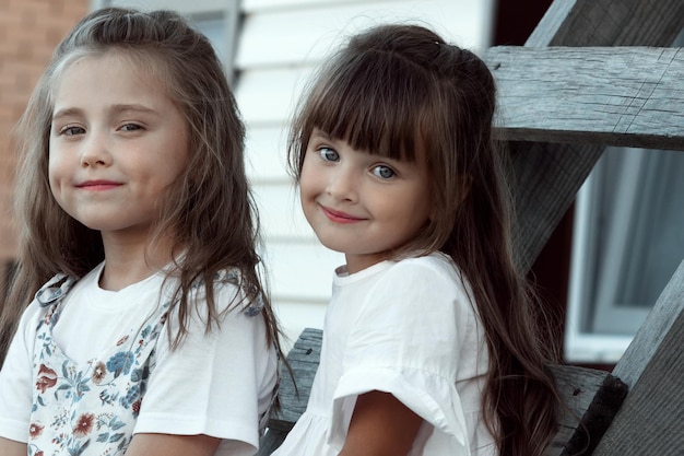 Dos chicas lindas y adorables están sentadas juntas en una escalera de madera Amistad infantil