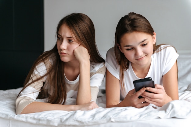 Dos chicas lindas teengae tendido en la cama, sosteniendo teléfonos móviles en casa