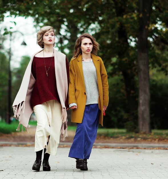 Dos chicas de moda alegre en el parque de otoño