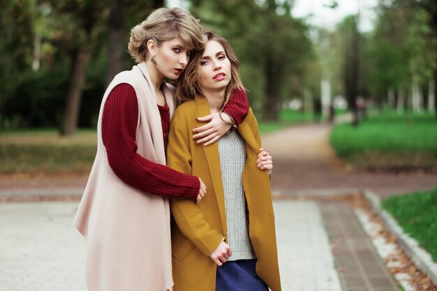 Dos chicas de moda alegre en el parque de otoño