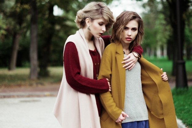 Dos chicas de moda alegre en el parque de otoño