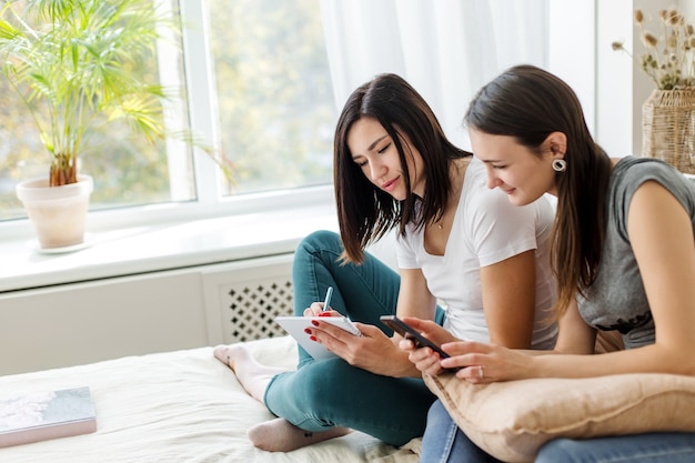 Dos chicas morenas están sentadas hablando, sosteniendo un libro y un teléfono.