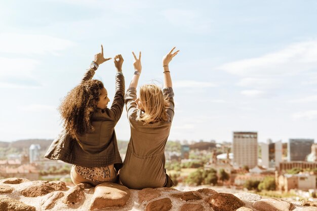 Dos chicas mostrando signos de amor usando sus dedos y disfrutando del concepto del horizonte de la ciudad