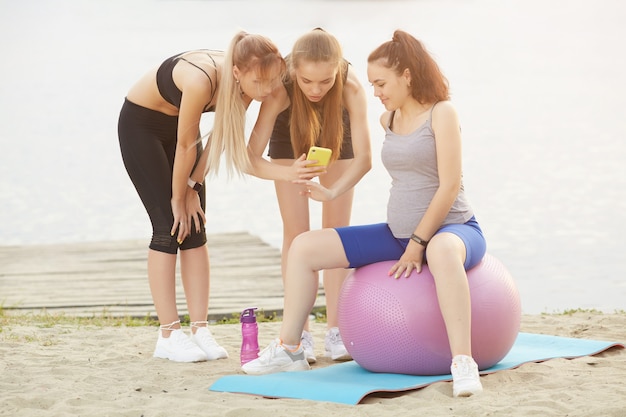 Dos chicas muestran a su amiga embarazada cómo hacer un ejercicio adecuado en una pelota de gimnasia