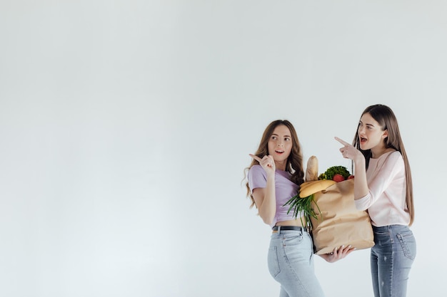 dos chicas pensando qué comprar en un fondo blanco con una canasta y un paquete de comida