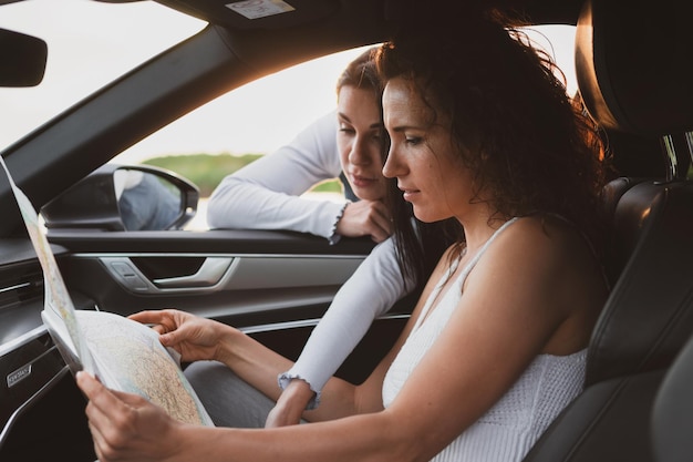 Dos chicas recorren las carreteras en un auto miran el mapa Concepto de vacaciones