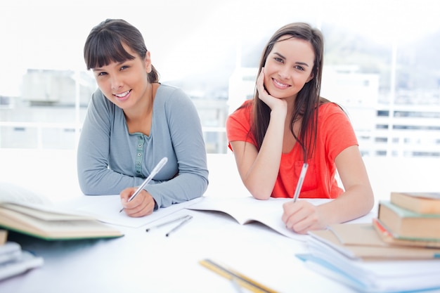 Dos chicas sonriendo y mirando a la cámara mientras hacen la tarea