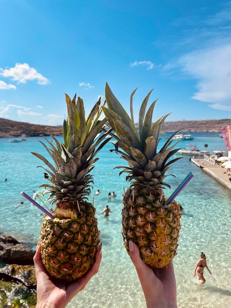 Foto dos chicas sosteniendo cócteles en una piña en la playa