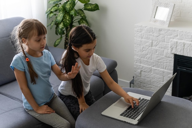 Dos chicas trabajando en una laptop, sonriendo y una hermana mayor ayudan a las más jóvenes.