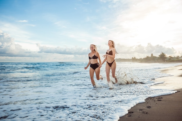 Dos chicas en traje de baño corren por la playa.