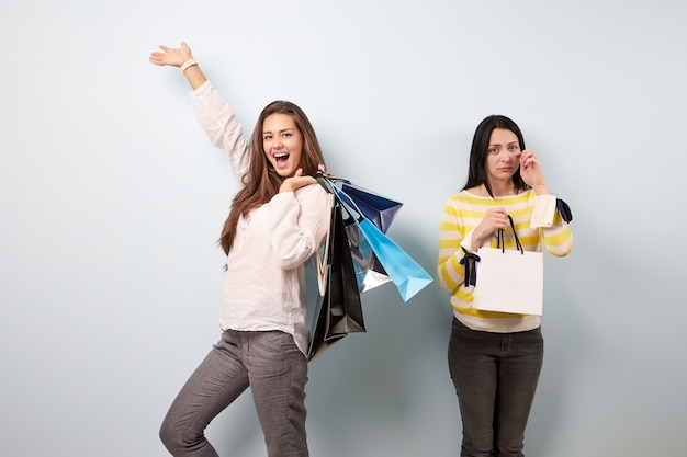 Dos chicas vestidas con ropa bonita y elegante después de ir de compras. Uno de ellos es feliz tiene muchas bolsas y otro tristemente solo sostiene una bolsa.