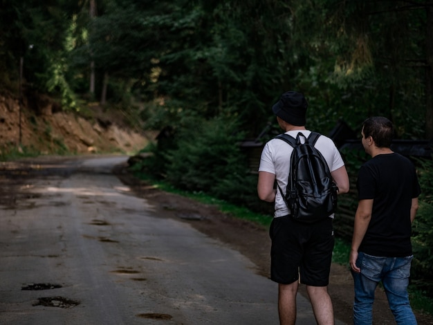 Dos chicos, uno con una camiseta negra y el otro con una blanca, caminan por un camino forestal.