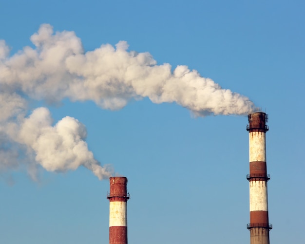 Dos chimeneas de fábrica con nubes de vapor o humo en el cielo azul. Contaminación ambiental.