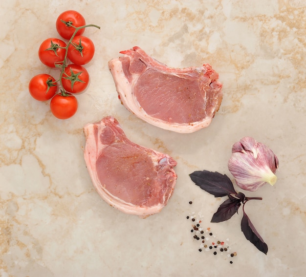 Dos chuletas de cerdo cruda en una mesa de mármol con tomates