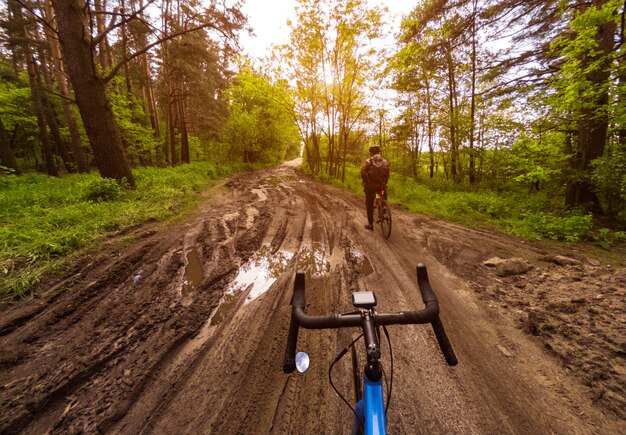 Dos ciclistas en bicicletas de grava en un bosque en un camino de tierra con charcos