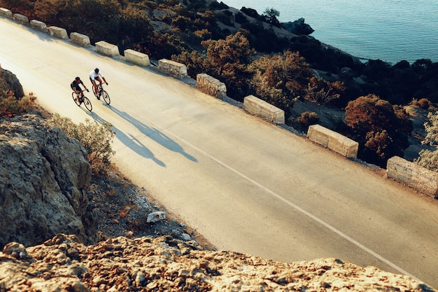 Dos ciclistas profesionales masculinos montando sus bicicletas de carreras en la mañana juntos en la carretera costera