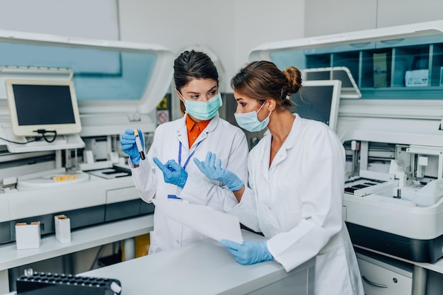 Dos científicas o técnicos con máscaras protectoras faciales trabajan en laboratorio con muestras de sangre humana.