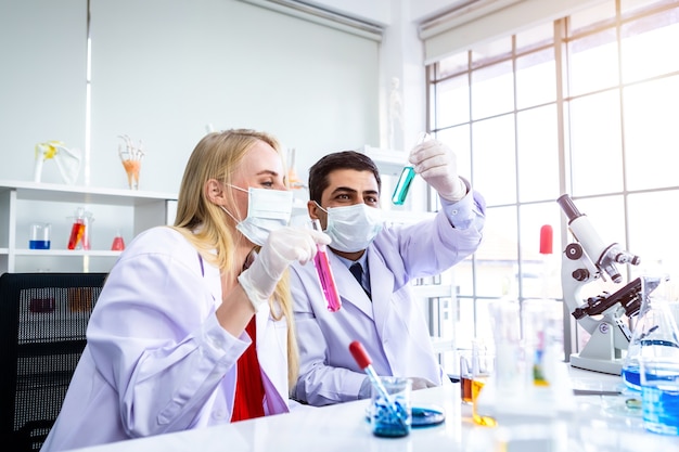 Dos científicos están trabajando sosteniendo mirando el tubo de ensayo con muestra en un científico de laboratorio de química o joven investigador femenino y masculino están haciendo investigaciones en el fondo de análisis de laboratorio