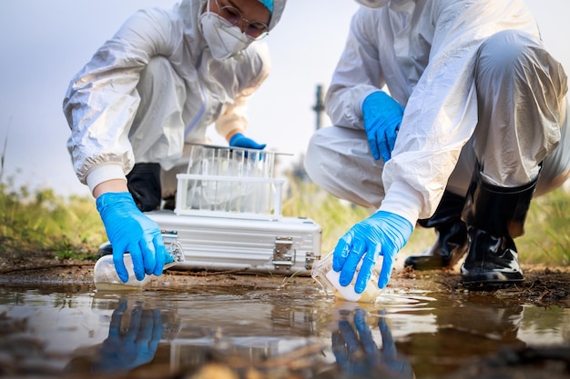 Dos científicos con trajes protectores y máscaras tomaron una muestra de agua para analizarla Concepto de problema ambiental Concepto de problema ambientalxDxA