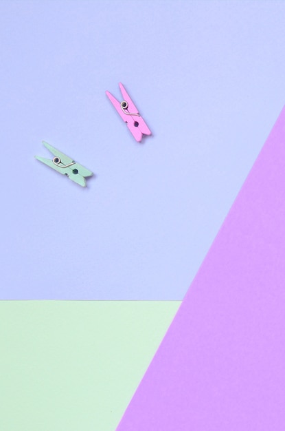 Dos clavijas de madera de colores se encuentran en el fondo de textura de papel de colores violeta, turquesa y rosa pastel de moda