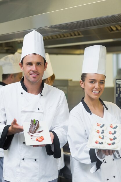 Foto dos cocineros felices que presentan platos de postre