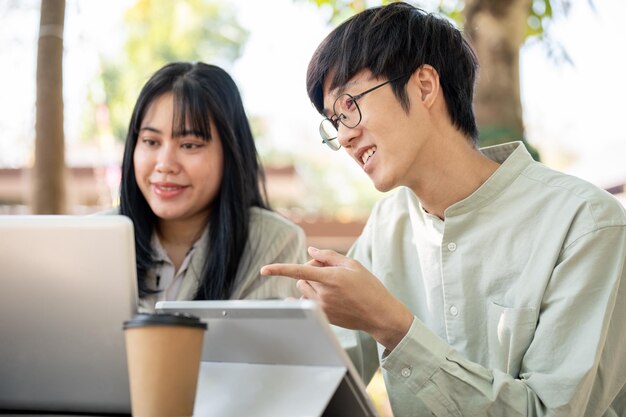 Dos colegas asiáticos, un hombre y una mujer, están discutiendo y colaborando en el trabajo juntos en un café.