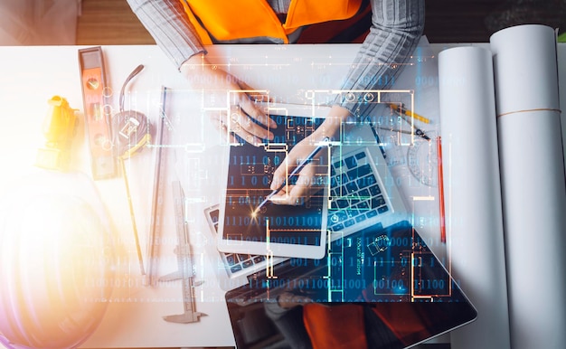 Dos colegas discuten el trabajo de datos y una tableta portátil con un proyecto arquitectónico en el sitio de construcción en el escritorio de la oficina