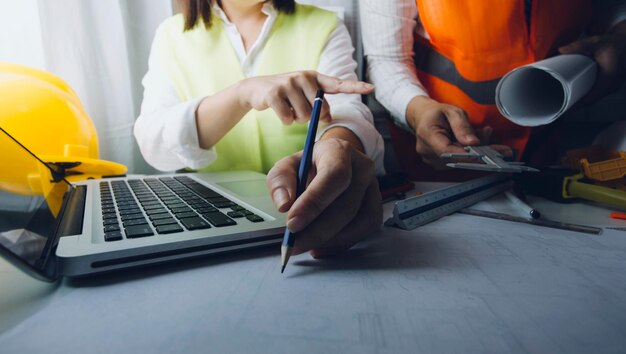 Dos colegas discutiendo el trabajo de datos y la tableta portátil con un proyecto arquitectónico en el sitio de construcción en el escritorio de la oficina