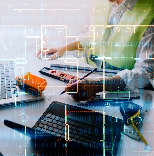 Dos colegas discutiendo el trabajo de datos y la tableta portátil con un proyecto arquitectónico en el sitio de construcción en el escritorio de la oficina