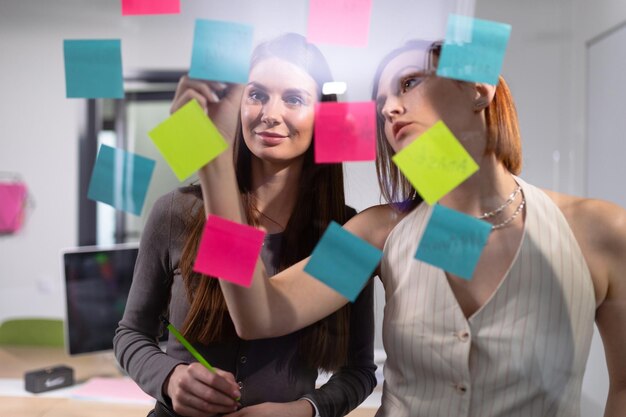 Foto dos colegas femeninas escriben planes de empresa en pegatinas de colores