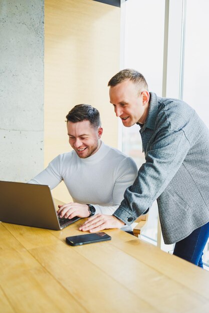 Dos colegas masculinos mientras trabajan con una computadora portátil en la oficina Dos empresarios orientados a objetivos colaboran en un espacio de trabajo moderno Dos jóvenes empresarios trabajan en una oficina luminosa