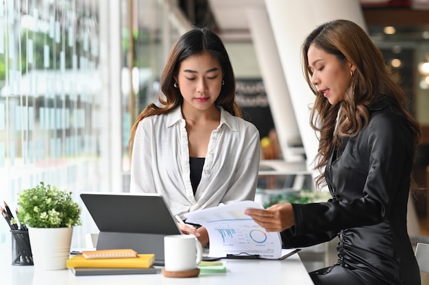 Dos colegas mujeres que trabajan junto con la tableta de la computadora en la sala de reuniones.