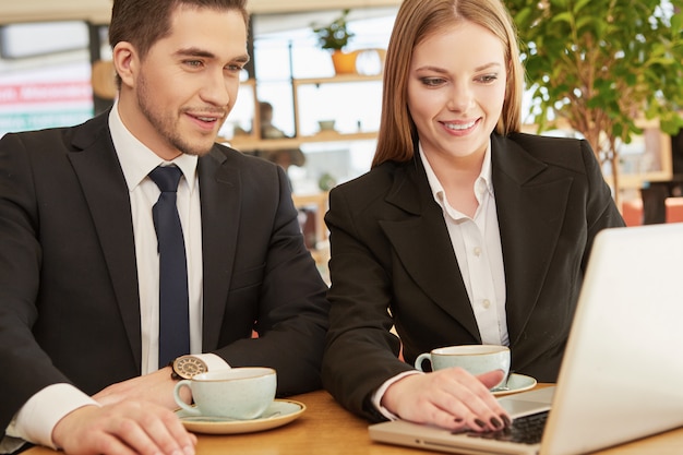 Dos colegas de negocios usando una computadora portátil en el café