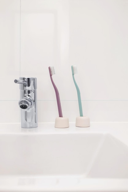 Dos coloridos cepillos de dientes ecológicos sostenibles en un lavabo blanco en el fondo del baño con espacio de copia Tema de problemas de higiene bucal Interior mínimo de la casa Ideas de publicidad de ortodoncia dental