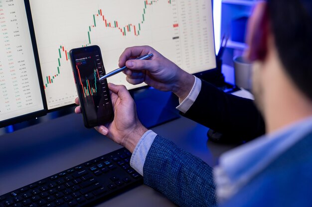 Foto dos comerciantes de bolsa de valores investigando datos en teléfonos inteligentes y portátiles vendibles