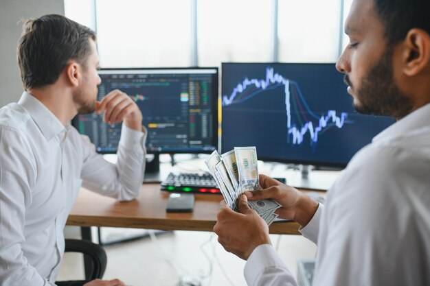 Dos comerciantes exitosos sentados en la oficina y mirando la pantalla revisando los datos de información de criptomonedas en el gráfico del mercado financiero que apunta en el monitor