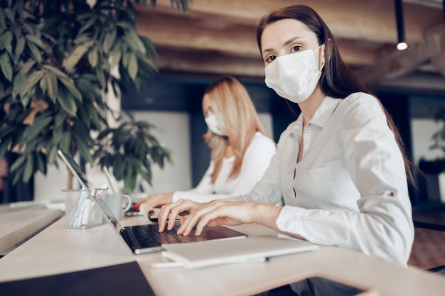 Dos compañeras que trabajan en la oficina juntos vistiendo máscaras médicas