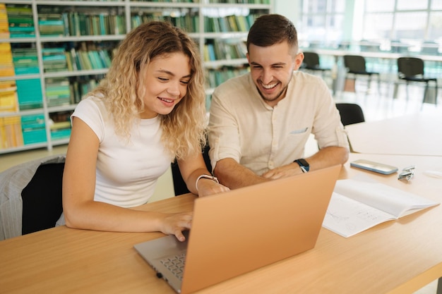 Dos compañeros de clase miran la computadora portátil y se ríen Niño y niña estudian en la biblioteca Concepto universitario