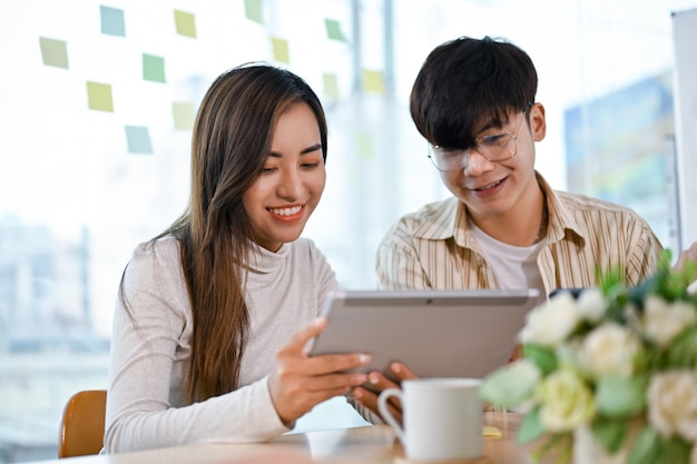 Dos compañeros de trabajo asiáticos, hombres y mujeres, disfrutan mirando juntos algo en la pantalla de la tableta