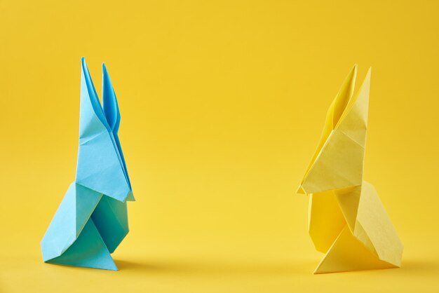 Dos conejos de pascua de origami de papel de colores sobre una superficie amarilla