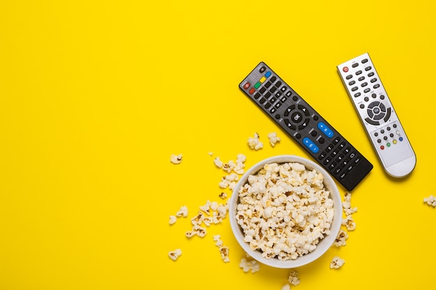 Dos controles remotos del televisor, sintonizador de TV y un tazón de palomitas de maíz en amarillo