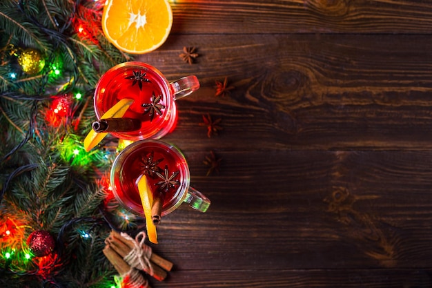 Dos copas de calentamiento invernal bebida caliente roja Navidad vino caliente sobre fondo de madera con sliceanise de naranja y palitos de canela