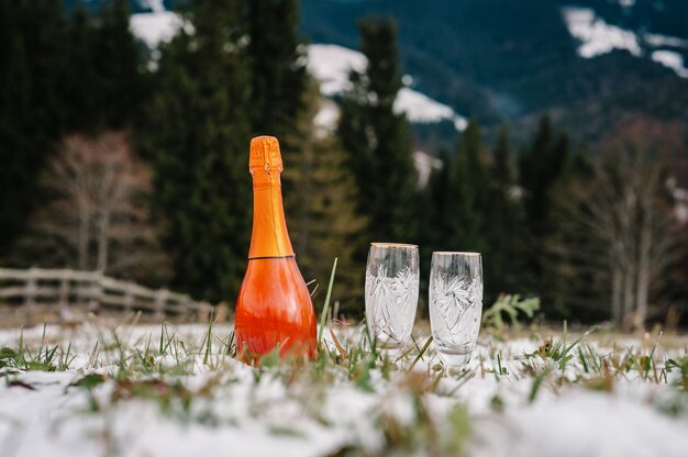 Dos copas de champán y una botella de vino espumoso en la nieve en la montaña.