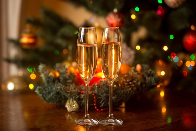 Dos copas de champán y corona de Navidad con velas en la mesa de madera