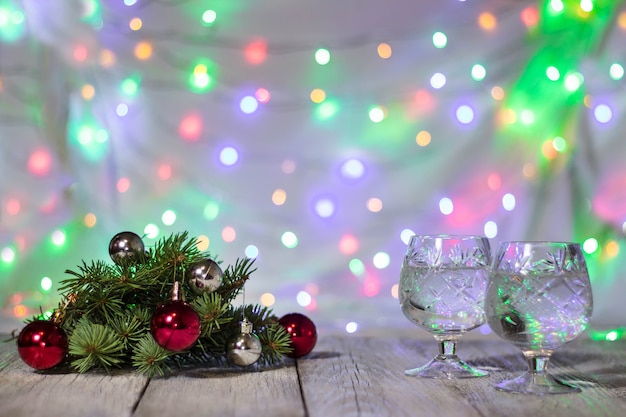 Dos copas de champán navideño con árbol de Navidad decorado con bolas rojas y plateadas contra el fondo bokeh claro.