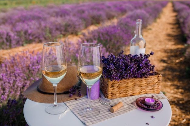 Dos copas de vino blanco y una botella en un campo de lavanda en Provance Flores violetas en el fondo