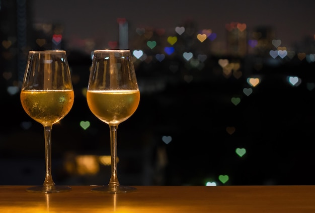 Foto dos copas de vino blanco con colorida forma de amor bokeh de la luz de la ciudad