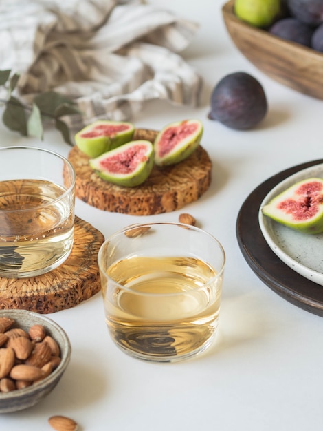 Dos copas de vino blanco, higos y almendras sobre un fondo blanco.